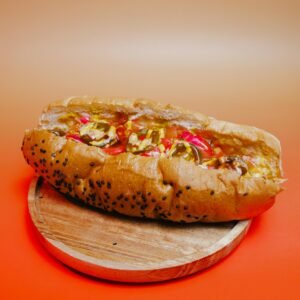 Foto de Ramon Hernandez A savory hot dog with toppings on a sesame seed bun, styled on a wooden plate with a warm background.
