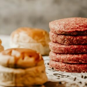 Foto de Jonathan Borba A stack of fresh raw beef patties with nearby burger buns, ready for cooking.
