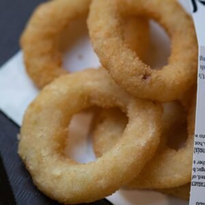 Foto de Valeria Boltneva Golden brown onion rings on paper, highlighting their crispy texture.