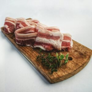 Sliced bacon laid on a rustic wooden board with herbs, showcasing a delicious and inviting food presentation.