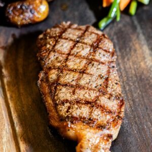Juicy grilled steak served with assorted roasted vegetables on a rustic wooden board.